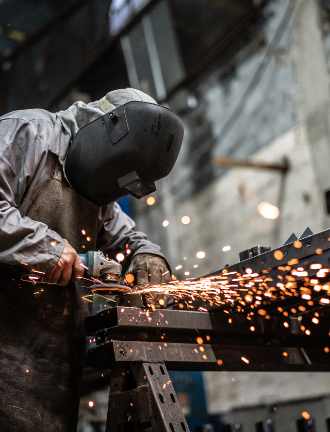 Worker in protective gear using a grinder, creating sparks in a workshop.