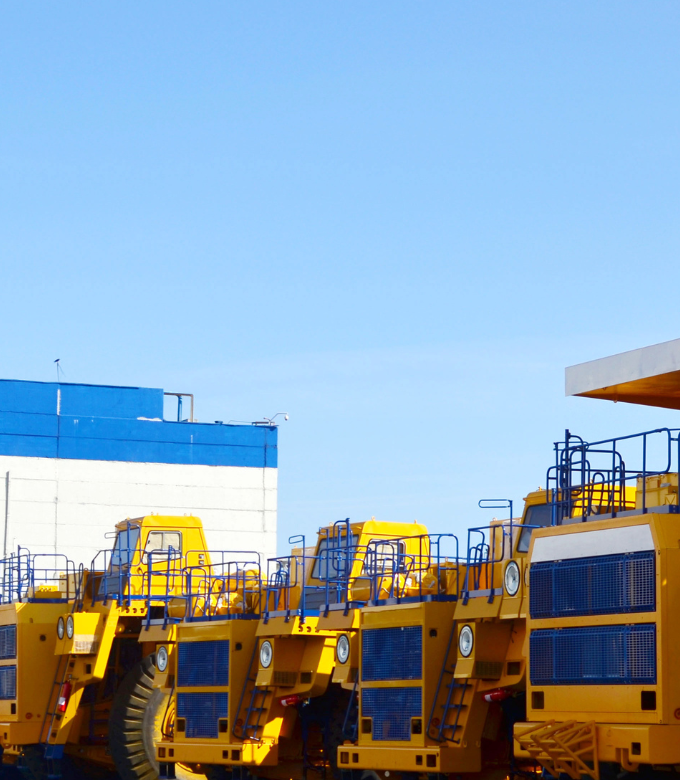 Row of large yellow industrial trucks parked in front of a blue and white building under a clear sky.