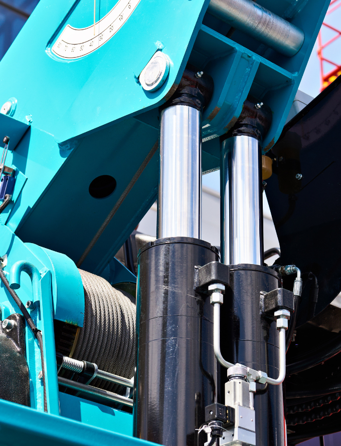 Close-up of hydraulic cylinders and machinery parts on a bright blue industrial machine.